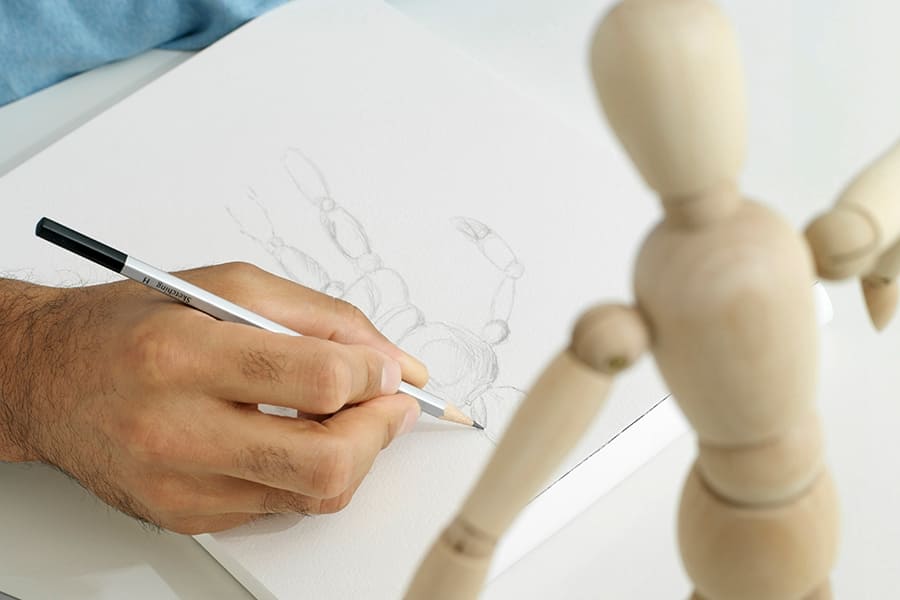 une personne dessine sur une feuille un croquis d'un mannequin en bois